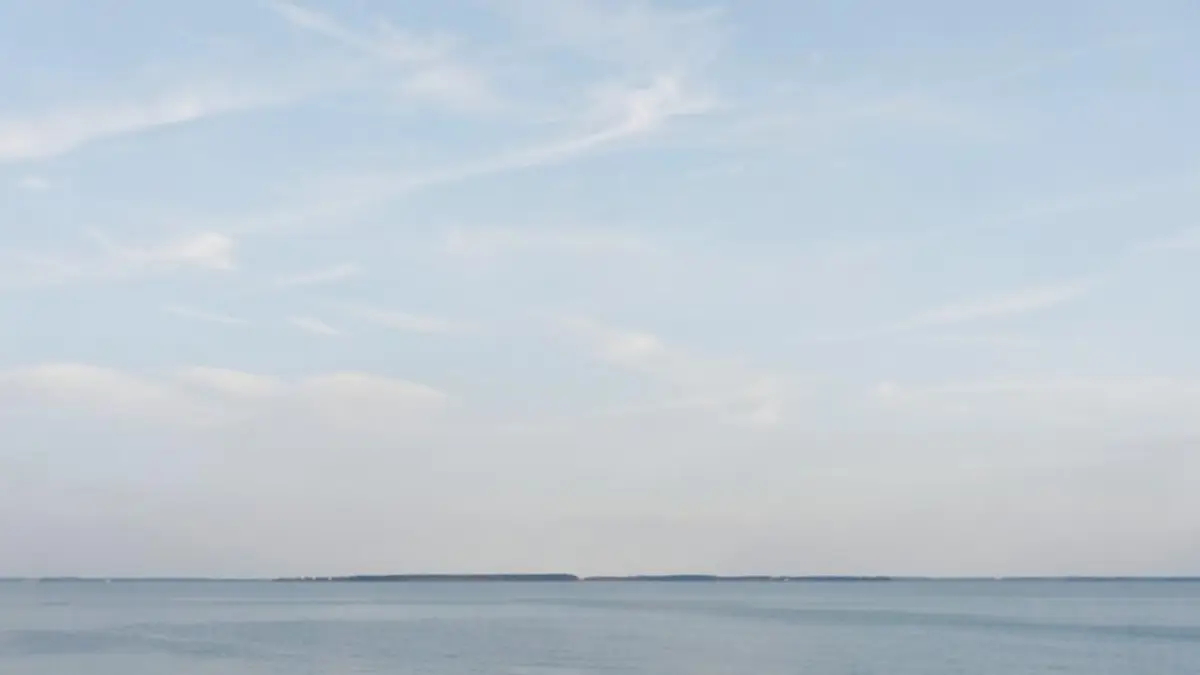Open pale sky with thin clouds above a distant, still horizon