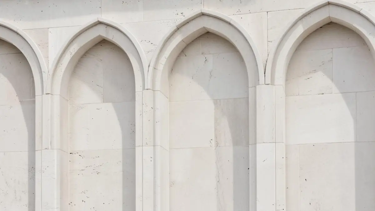 Detail of a pale stone facade with repeating arches and soft shadow
